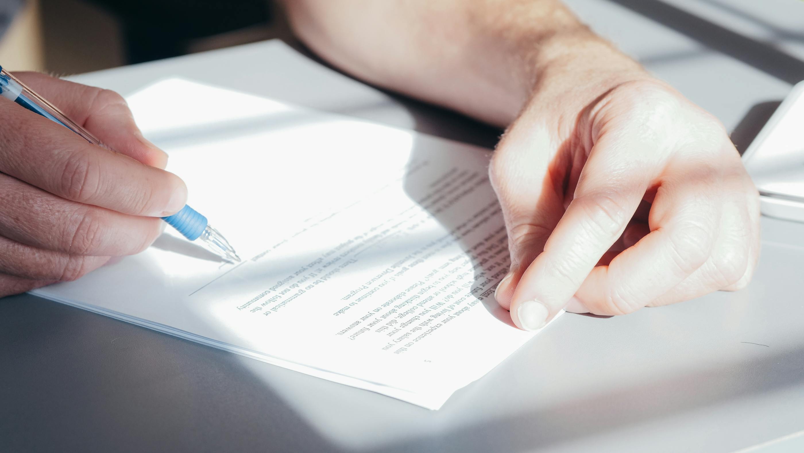 Illustrative close-up of a person signing a document on an office desk