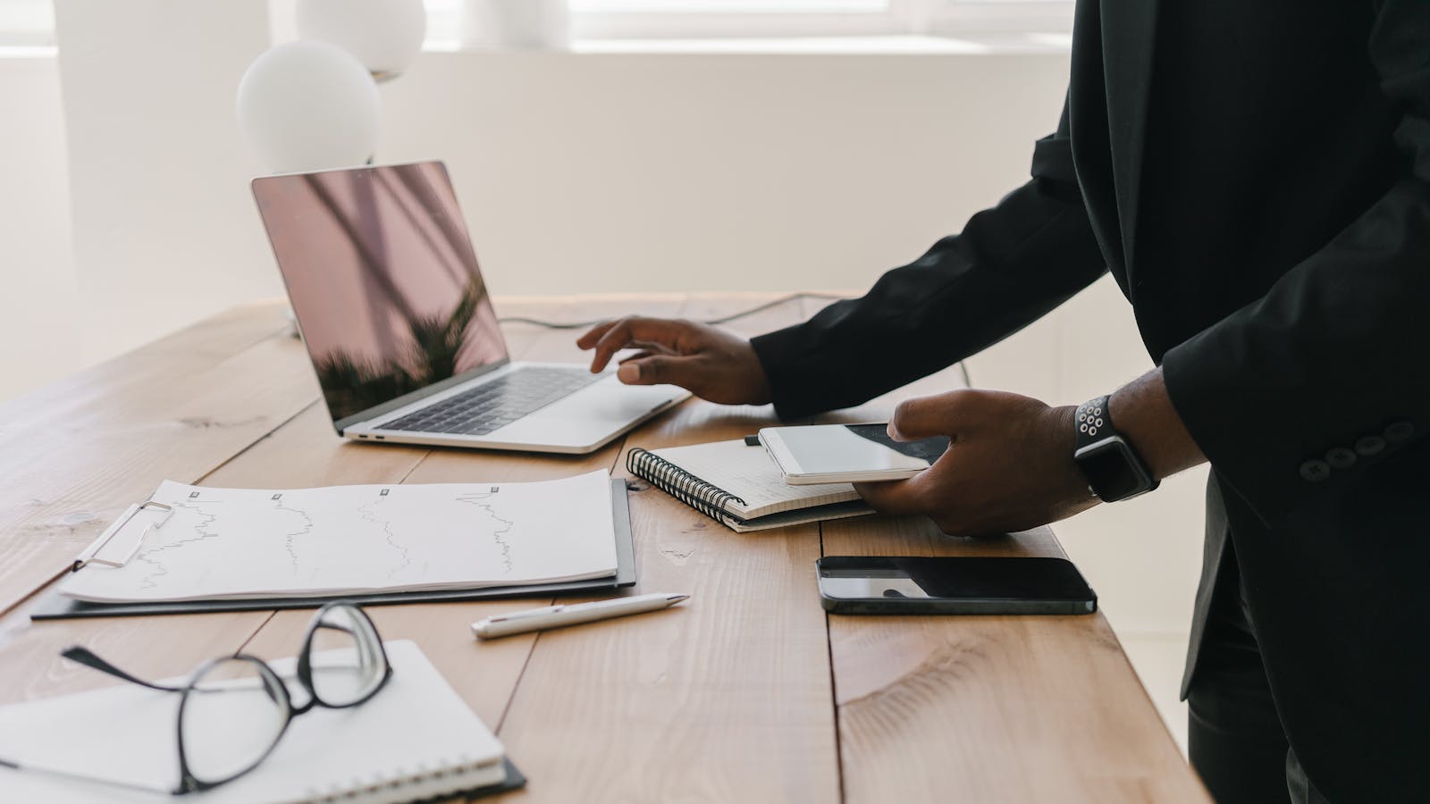 Professional using a laptop beside paperwork and a notebook